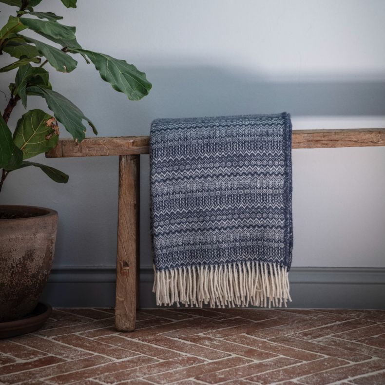 Blue and cream Fair Isle patterned woven throw blanket with tasselled fringe, draped over a rustic wooden bench to showcase the traditional knit-inspired design and soft textured fabric.