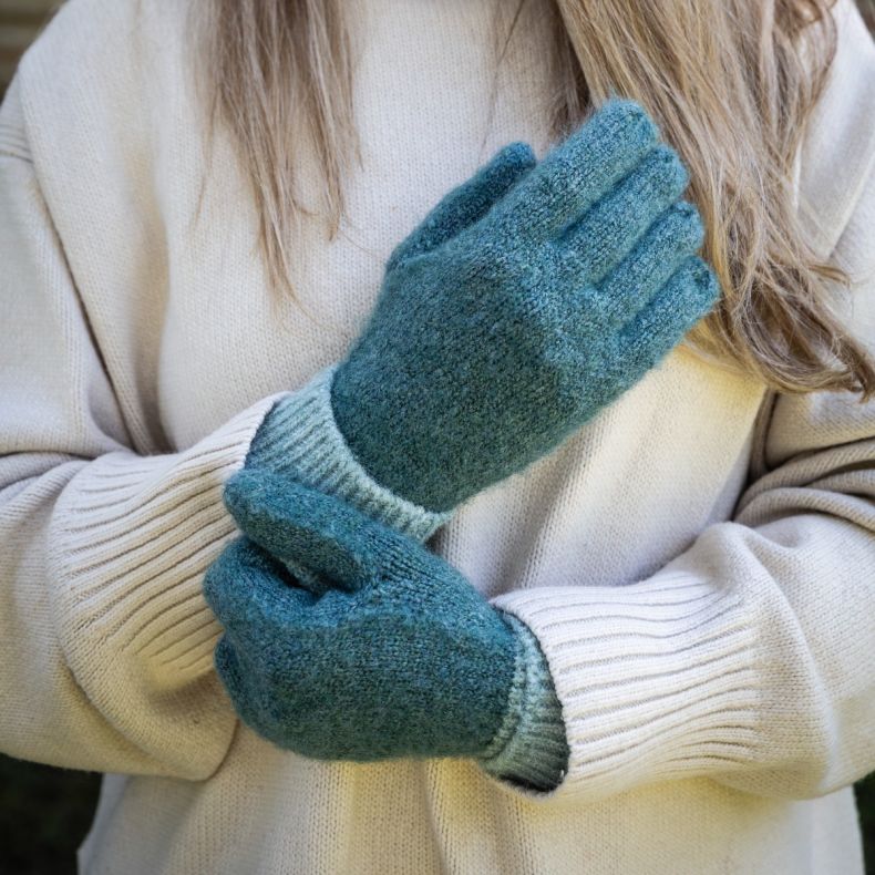Green and pale mint colour-block knitted gloves with ribbed cuffs, shown worn with a cream knit jumper to highlight the soft textured fabric, contrasting tones and cosy winter styling.