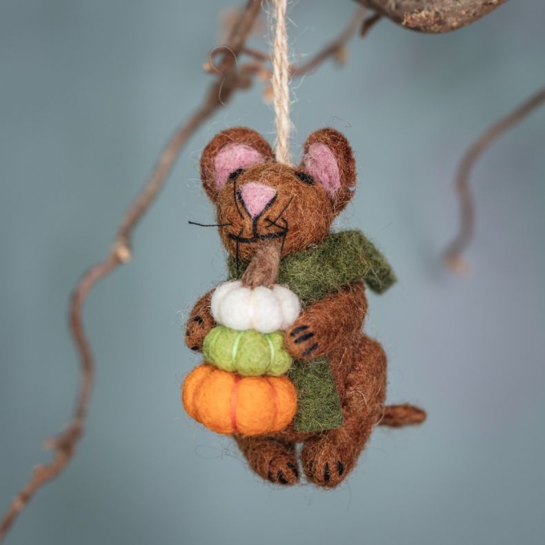 Felt hanging mouse ornament wearing a green scarf and holding stacked white, green and orange pumpkins, suspended by a natural hanging loop and displayed on a decorative branch.