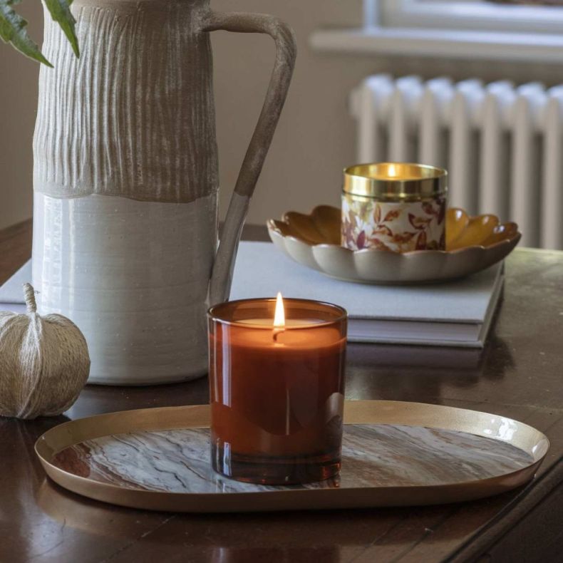 orange and cedar candle in burnt orange glass jar on a marble tray