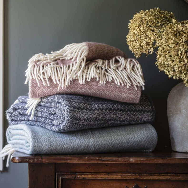 Pink fair isle wool throw on top of a selection of blue wool throws. 