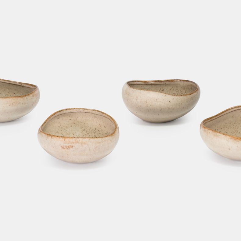 Set of four oatmeal-coloured ceramic bowls with a speckled glaze finish and organic, asymmetrical shape. Displayed separately to showcase their handcrafted design, the bowls feature soft neutral tones, textured interiors and gently curved rims against a p