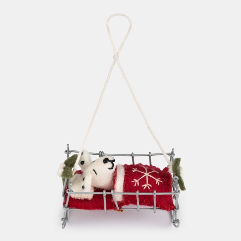 Felt Dalmatian puppy Christmas hanging decoration in a miniature silver-tone wire bed, featuring a white wool-effect puppy with black spots and embroidered facial details, tucked beneath a red felt blanket with white snowflake embroidery and holly leaf ac