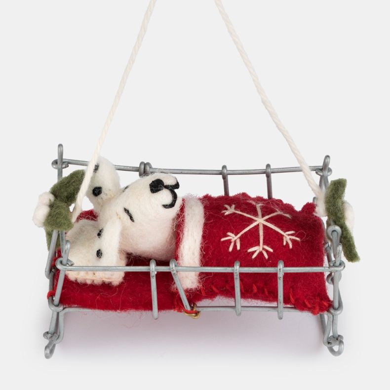Felt Dalmatian puppy Christmas hanging decoration shown in a close-up view, featuring a white wool-effect puppy with black spots and embroidered facial details, tucked beneath a red felt blanket with white snowflake embroidery in a silver-tone wire bed wi
