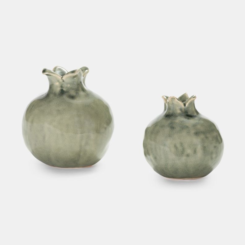 Set of two decorative pomegranate-shaped ceramic ornaments in a soft sage green glaze. Displayed side by side in different sizes, each ornament features a rounded form, subtle textured detailing and a sculpted crown, shown against a plain light grey backg