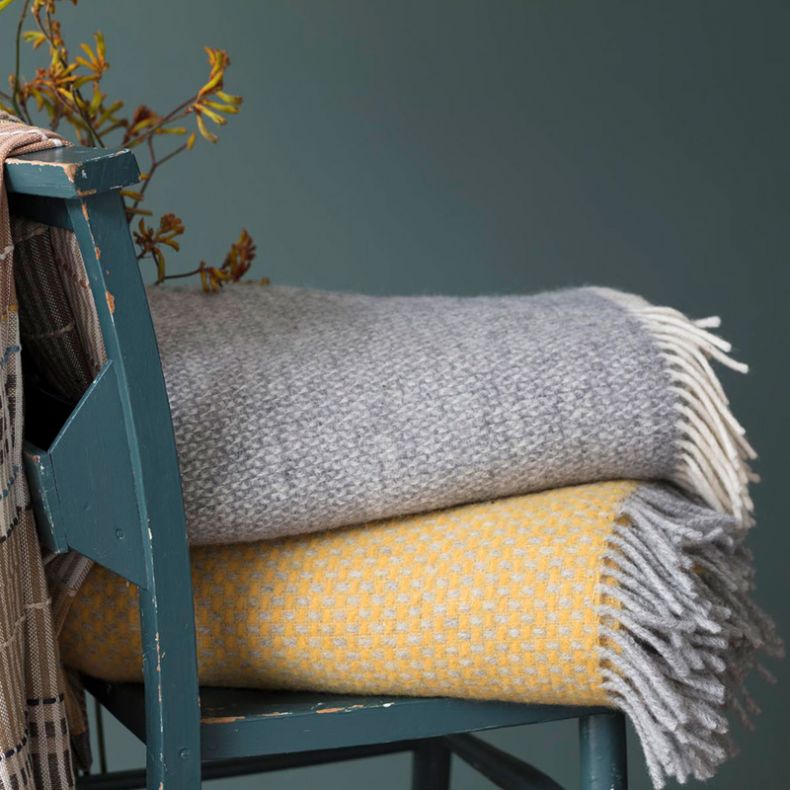 Folded grey and yellow wool blankets stacked on a distressed teal chair.









