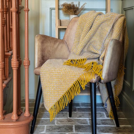 Ochre National Trust woven blanket with a soft texture and fringe on one edge, displayed draped over a chair.