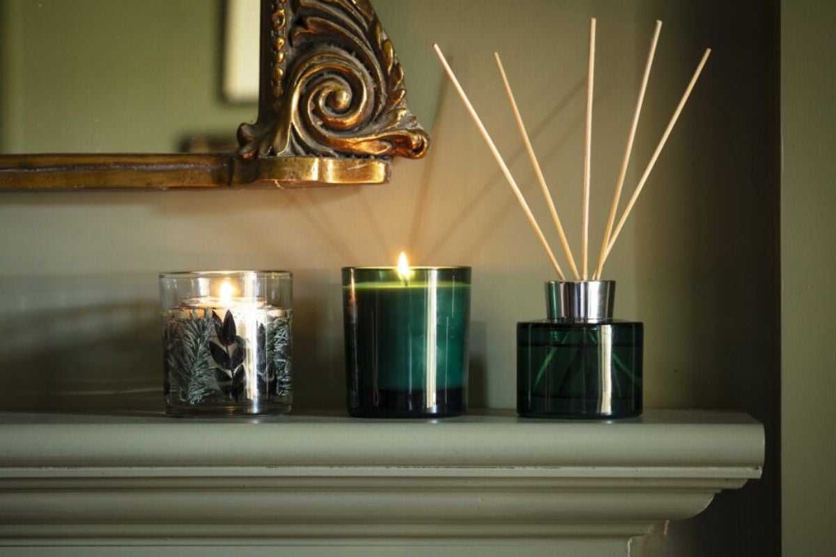 Candles and reed diffuser on a mantelpiece creating a warm, inviting glow – part of the National Trust autumn winter home fragrance and accessories collection.