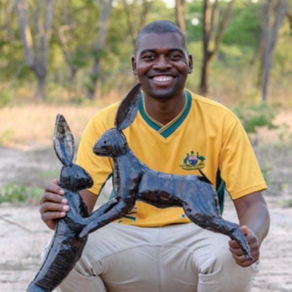 A man in a yellow shirt smiles while holding a metal sculpture of Chi Africa boxing hares.