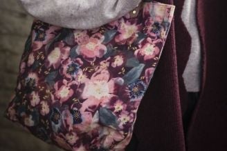 Bags - Woman wearing a National Trust crossbody bag with a colourful floral print, standing in a bright, leafy setting.