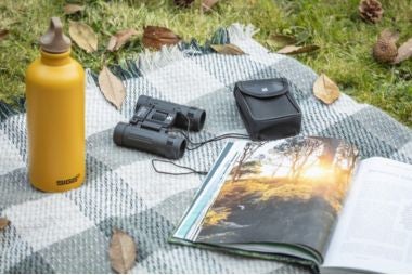 All outdoor accessories - picnic rug with guide boo, water bottle and binoculars set out on the grass on a Autumn day